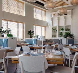 A wide view of Saltwater Coastal Grill. Glass light fixtures evoking fish scales hang from the cieling. Blue accents and greenery are interspersed throughout the breezy space